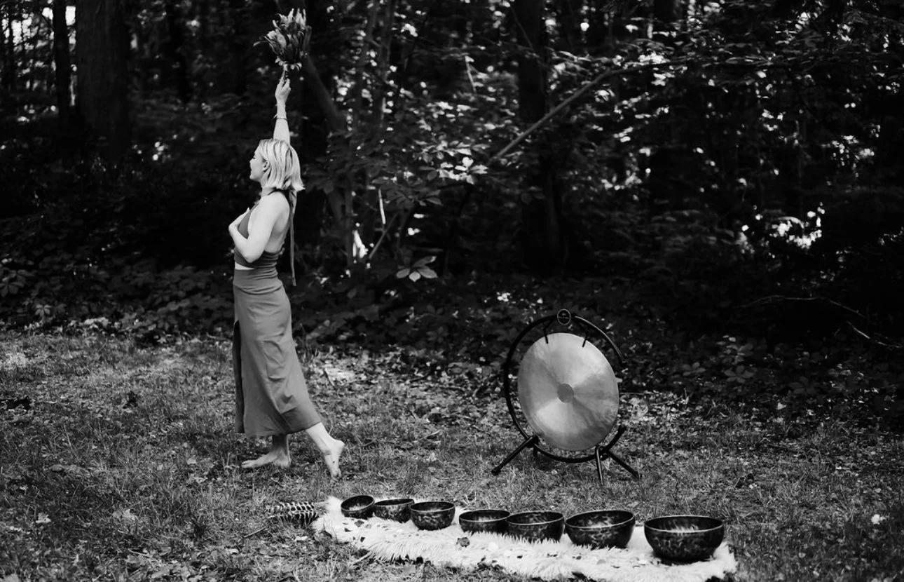 Christina standing among crystal singing bowls and a gong in the forest