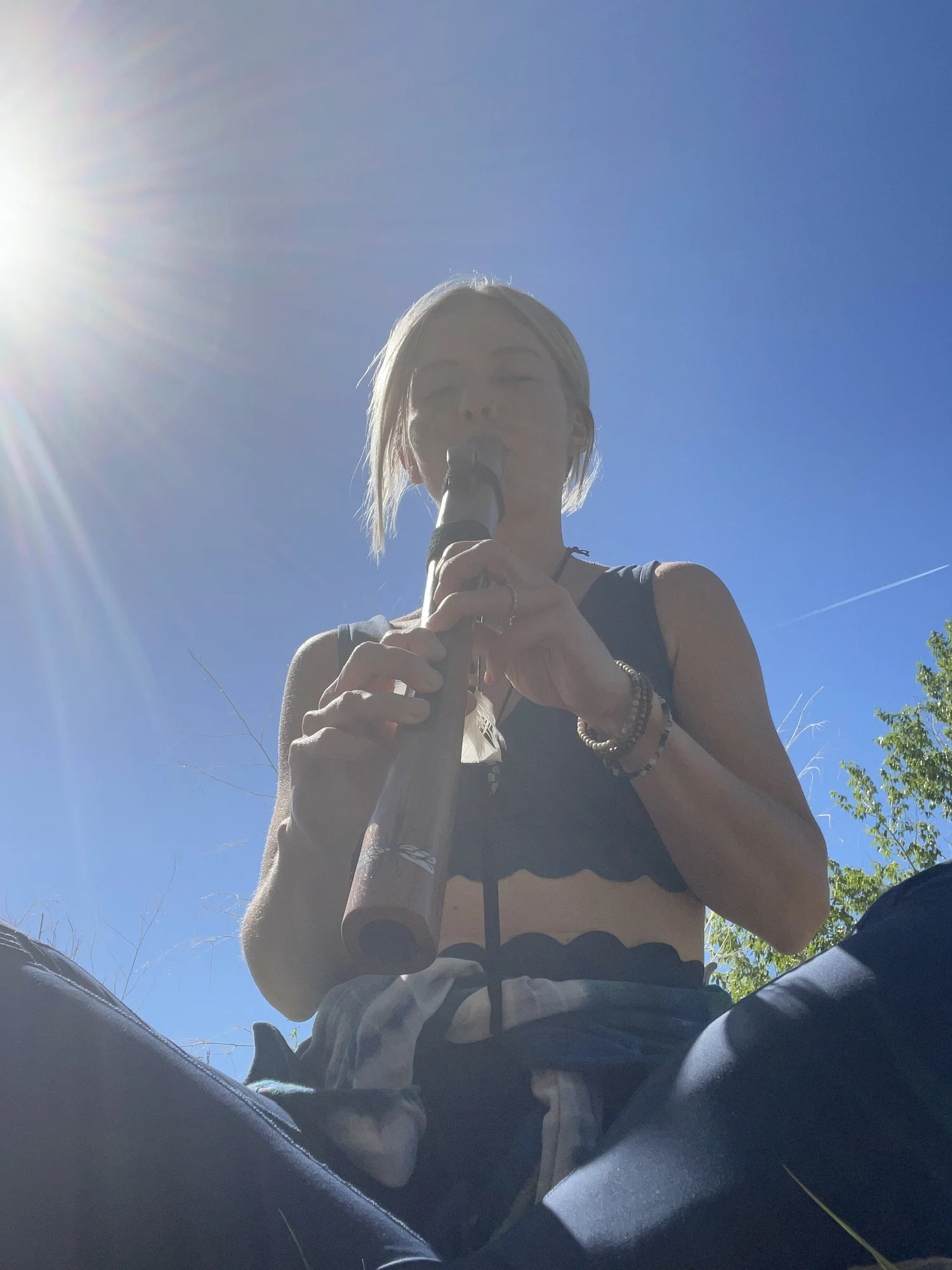 Christina playing a wooden flute outdoors under a blue sky