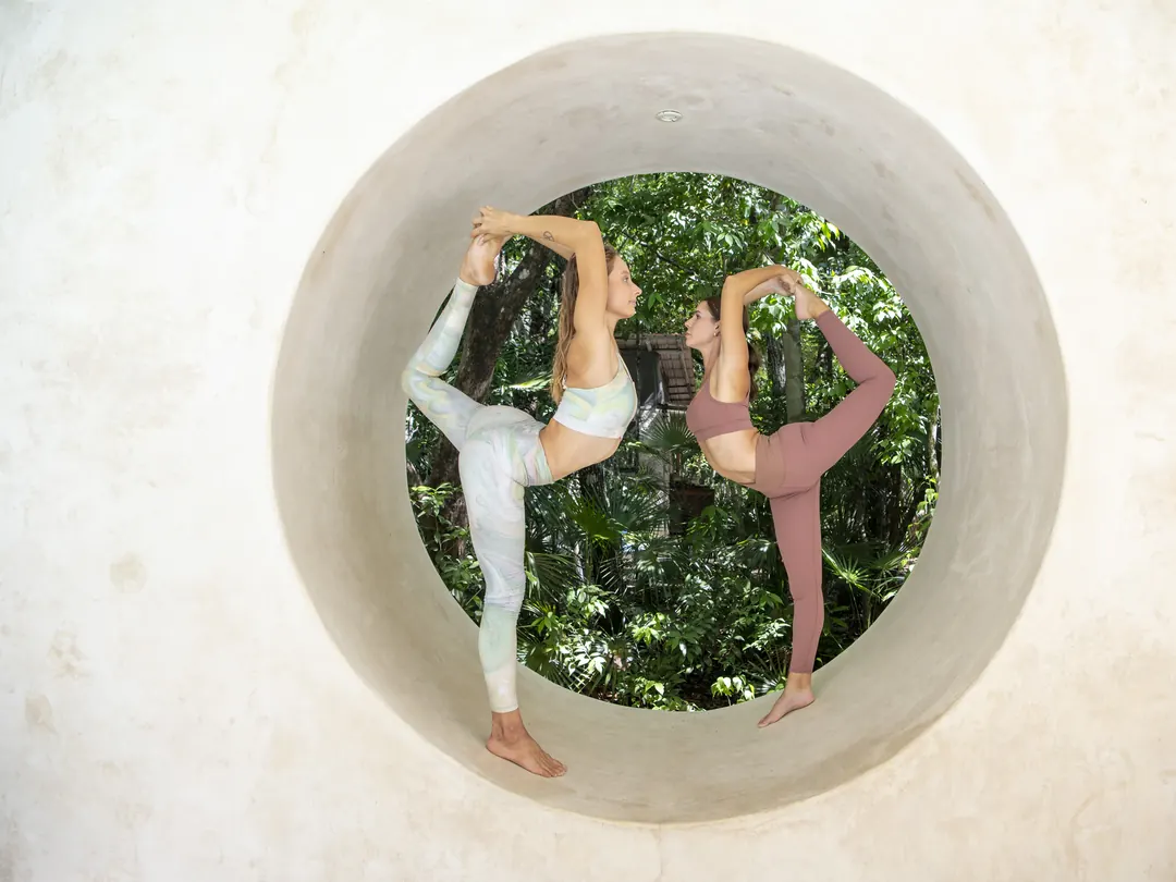 Two women in a dancer pose inside a round jungle window