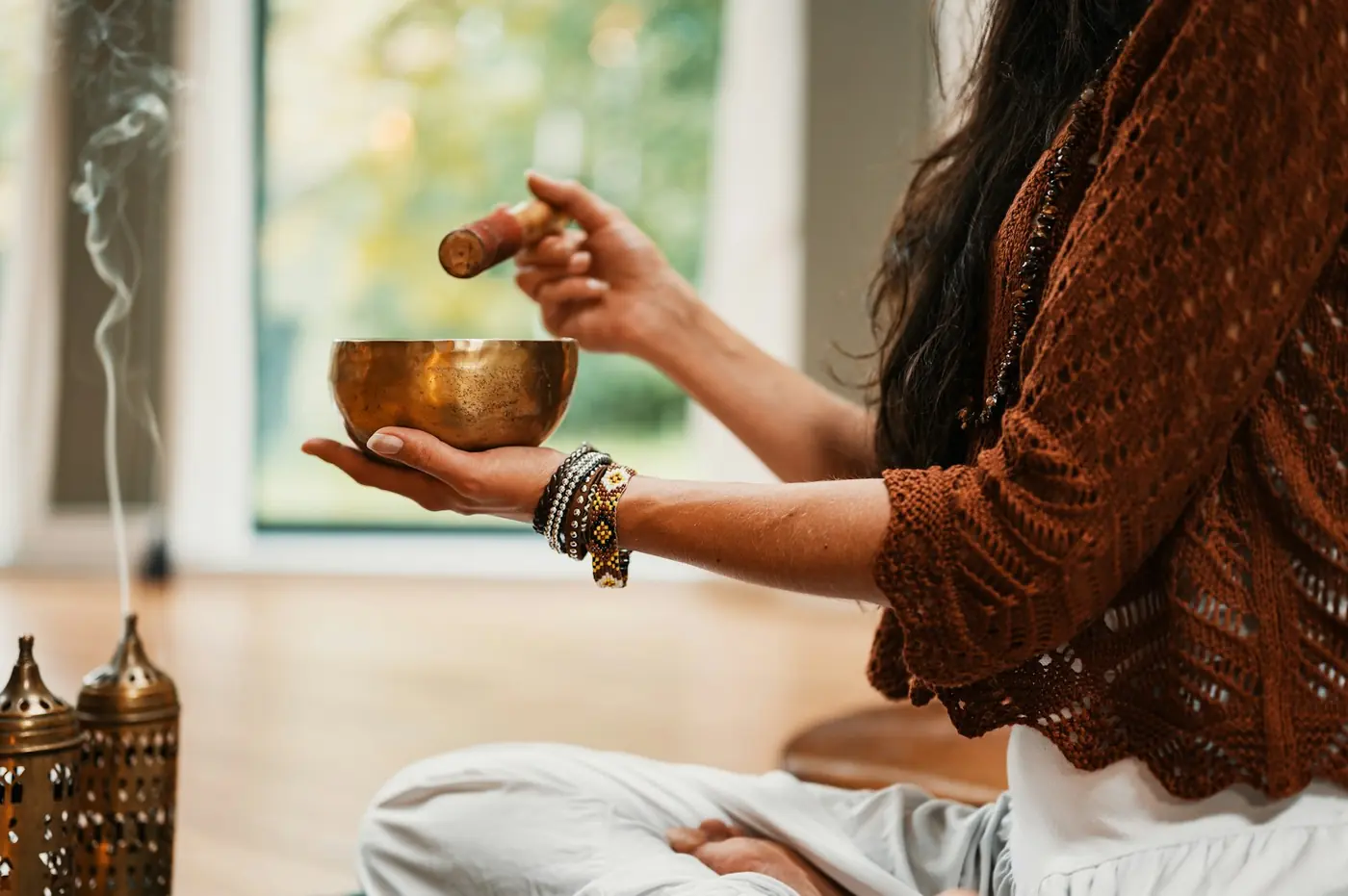 Hands holding a singing bowl beside a curl of incense smoke