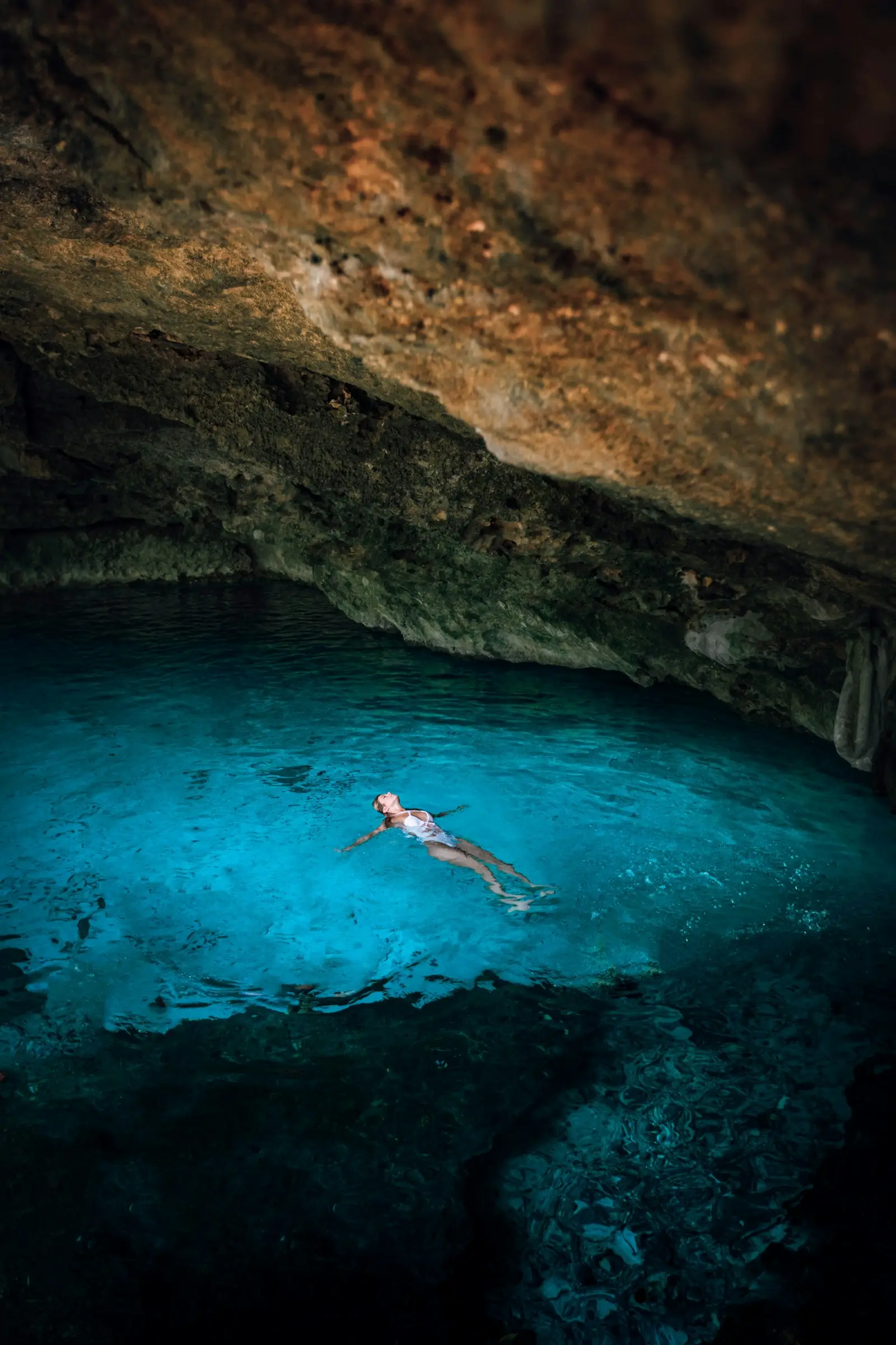 A swimmer floating in clear blue water inside a cave